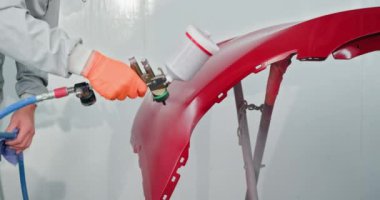 Bir araba boyacısı, bir otomotiv dükkanındaki kırmızı tamponu tamir ediyor ve boyuyor. Bir haznede sprey tabanca kullanıyor. Otomotiv boyama servisi. Araba Boyacısı Oto Servisi 'nde Kırmızı Tampon Tamiri