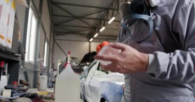 Koruyucu giysili teknisyen elinde boya tabancasıyla araba tamir atölyesinde araba boyamaya hazırlanıyor. Otomobil tamircisi atölyede boya tabancası tutuyor. Otomobil tamirhanesinde boyacı.