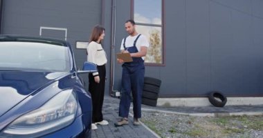 Panosu olan erkek tamirci ve bayan müşteri ya da araba sahibi atölyede işin kapsamını tartışıyor. Otomobil servisi, onarım, bakım ve insan konsepti.