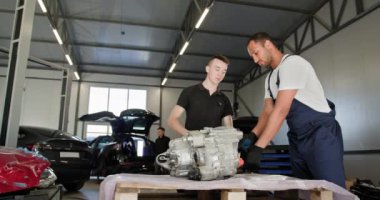 Tamirci, elektrikli araba motoru tamir ediyor. Modern bir oto tamir atölyesinde parçalanmış elektrikli araba motoru üzerinde çalışan iki erkek tamirci. Ekip aracın bakımını ve onarımını yapıyor.
