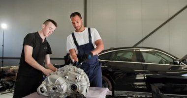 Tamirci, elektrikli araba motoru tamir ediyor. Modern bir oto tamir atölyesinde parçalanmış elektrikli araba motoru üzerinde çalışan iki erkek tamirci. Ekip aracın bakımını ve onarımını yapıyor.