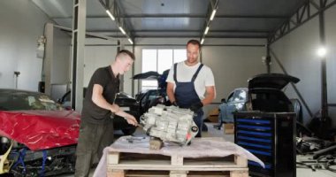 Tamirci, elektrikli araba motoru tamir ediyor. İki tamirci garajda parçalanmış bir elektrikli araba motoru üzerinde çalışıyor. Aracı tamir ediyor ve bakımını yapıyorlar. Her şeyin düzgün çalışmasını sağlıyorlar.