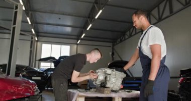 EV servisi, elektrikli araba motoru. Profesyonel bir atölyede elektrikli araba motoru tamir eden iki tamirci. Elektrikli araç parçalarının bakımı ve bakımı. Tamirci Elektrikli Araba Tamiri