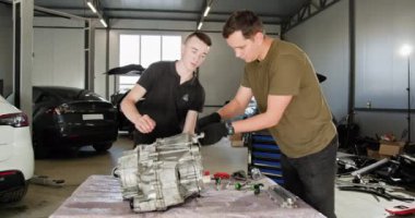 Modern bir oto tamirhanesinde elektrikli araba motorunun tamiri için işbirliği yapan iki tamirci. Gelişmiş otomotiv teknolojisi üzerine odaklanmış bakım çalışması. EV onarım ve servis kavramı.