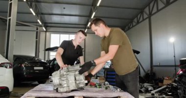 Bir oto hizmet atölyesinde kısmen parçalanmış bir elektrikli araba motoru üzerinde çalışan iki tamirci modern elektrikli araçların bakımını ve tamirini sergiliyor. EV onarım ve servis kavramı.