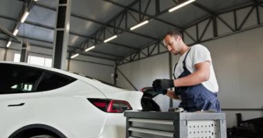 Teknisyen EV Araba Batarya Hücre Modülü 'nde sorun çıkarıyor. Bir erkek teknisyen bir EV araba akü hücresi modülünü vuruyor. Tamirci bir atölyede voltmetreyle araba motorunu inceliyor..
