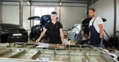 Teknisyen EV Araba Batarya Hücre Modülü 'nde sorun çıkarıyor. İki erkek teknisyen bir garajda elektrikli araba akü modülü üzerinde çalışıyor. Modern Ev Teçhizat ve Araçlarla Onarım Sahnesi.