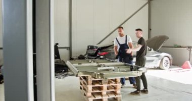 Teknisyenler atölyedeki EV Araba Batarya Modülünde sorun çıkarıyorlar. İki teknisyen, bir atölyede arabadan çıkarılan elektrikli bir aracın pil modülünü vuruyor..