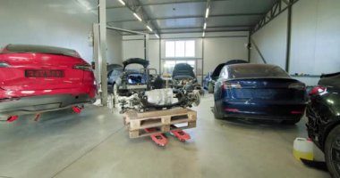 Modern bir otomotiv tamirhanesi elektrikli araba bakım ve onarım üzerine odaklanmış birkaç araba ve parçalanmış bir motorla. EV onarım konsepti. Otomobil Servisi, Elektrikli Araba Aküsü Taşıma.