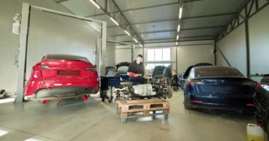 Modern bir oto tamirhanesinde elektrikli bir arabanın parçalanmış motoru üzerinde çalışan bir tamirci. Teknoloji ve uzmanlıkla EV bakım ve onarım konsepti. EV onarım konsepti. Otomatik Servis.