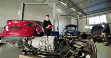 Bir tamirci modern bir oto tamirhanesinde parçalanmış bir elektrikli araba motorunu inceliyor. Görüntü, EV bakım ve servis sürecini vurgular. EV onarım konsepti. Otomatik Servis, Elektrik Motoru