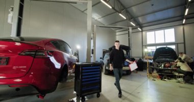 Tamirci modern bir oto tamirhanesinde elektrikli araba motorlarını kontrol ediyor. Görüntüde kırmızı bir elektrikli araba ve teknisyenler tarafından tamir edilen başka bir araba yer alıyor. EV onarım konsepti. Otomatik Servis, Elektrik Motoru