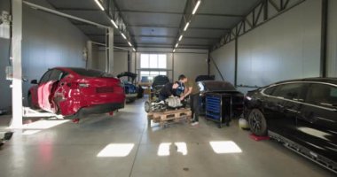 Modern bir atölyede parçalanmış elektrikli araba motoru üzerinde çalışan bir tamirci. EV bakım ve onarım devam ediyor. EV onarım konsepti. Otomobil servisi, elektrikli araç motor bakımı