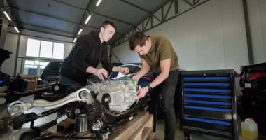 Modern bir otomotiv tamirhanesinde, EV bakım ve hizmet sunan parçalanmış bir elektrikli araba motoru üzerinde çalışan iki tamirci. EV onarım konsepti. Otomatik servis, elektrikli araç motoru