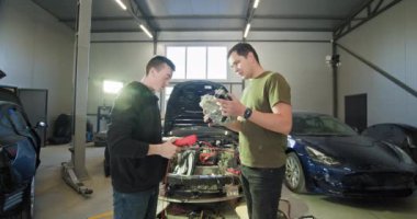 Modern bir otomobil benzin istasyonunda elektrikli araba motoru üzerinde çalışan iki tamirci. EV bakım ve onarım kavramı. EV onarım konsepti. Otomobil servisi, elektrikli araç motor bakımı