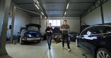 Modern bir oto tamirhanesinde elektrikli araçları tamir etmeye çalışan iki tamirci. EV bakım, servis ve onarım kavramı. EV onarım konsepti. Otomobil servisi, elektrikli araç motor bakımı