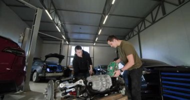 Profesyonel bir atölyede parçalanmış bir elektrikli araba motorunu tamir etmek için birlikte çalışan iki tamirci. Parçalarla ilgileniyorlar ve düzgün bakım sağlıyorlar. EV onarım konsepti. Otomatik Servis.