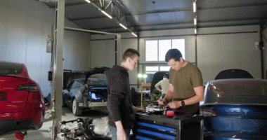 Otomobil tamirhanesinde parçalanmış bir elektrikli araba motoru üzerinde çalışan iki tamirci, EV bakım ve onarımına odaklanıyor. EV onarım konsepti. Otomobil servisi, elektrikli araç motor bakımı