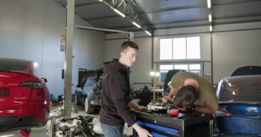 İki erkek tamirci modern bir otomobil atölyesinde elektrikli araba motoru tamirinde birlikte çalışıyorlar. Özelleştirilmiş aletler ve arka planda görünen elektrikli araçlar. EV onarım konsepti. Otomatik Servis