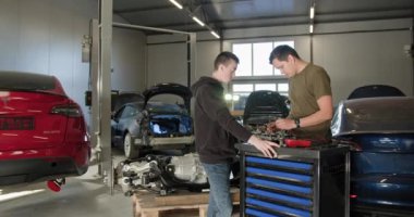 Erkek tamirciler profesyonel bir oto tamirhanesinde parçalanmış bir elektrikli araba motorunu tamir ediyorlar. EV onarım konsepti. Otomobil servisi, elektrikli araç motor bakımı