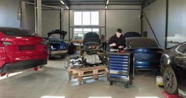 Modern bir tamir atölyesinde, EV bakım ve hizmet sunan parçalanmış bir elektrikli araba motoru üzerinde çalışan bir oto tamircisi. EV onarım konsepti. Otomobil servisi, elektrikli araç motor bakımı