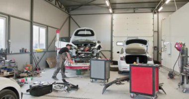 Modern, iyi donanımlı bir oto tamirhanesinde araba tamiri yapan bir tamirci. Görüntü, bir aracın gövdesini ve bileşenlerini düzeltmenin karmaşık sürecini gösteriyor. Otomobil Atölyesinde Tamirci Araba