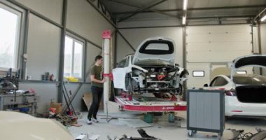 Bir teknisyen modern bir atölyede araba tamiratı yapıyor, elektrikli bir aracı tamir etmek için gelişmiş ekipman kullanıyor. Çeşitli alet ve makinelerle temiz ve iyi düzenlenmiş çalışma alanı.