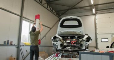 Modern, temiz bir atölyede araba tamircisi. Araba daha iyi erişim için asansörle yükseltildi. Modern Atölyede Araba Tamiri Teknisyeni