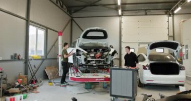 Temiz ve modern bir oto tamirhanesinde iki tamirci özenle çalışıyor. Bu görüntü profesyonel bir araba servisinin sürecini ve ortamını yakalar. Otomobil Atölyesinde Araba Tamiri