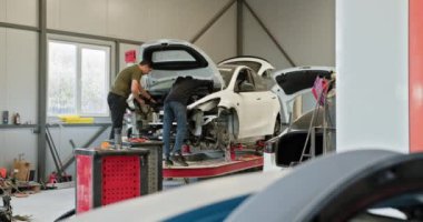 Temiz ve modern bir atölyede iki tamirci bir araba üzerinde çalışıyor. Araç asansörde, gövdesi ve elektriği tamir ediliyor. Modern bir atölyede Araba Tamirciliği