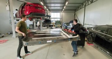 Modern bir otomotiv atölyesinde büyük bir elektrikli araba aküsünü idare etmek için birlikte çalışan iki teknisyen. Takım çalışması, onarım ve gelişmiş araç teknolojisi üzerinde duruluyor. Elektrikli araba, açılırken.