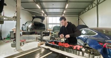 Erkek teknisyen, modern bir otomotiv atölyesinde elektrikli araba aküsü modülünü onarıyor. Tamir edilmeden önce kullanılmış bir Lityum iyon araba aküsü..