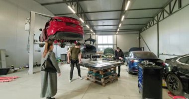 İyi donanımlı bir oto tamirhanesinde elektrikli araçlar üzerinde çalışan teknisyenler. Görüntü, akü modülleri ve çeşitli araçların bakım yapılmasını ön plana çıkarıyor. Elektrikli araba. Pil hücre modülü paketi