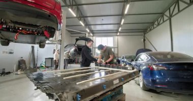 Modern bir araba tamir atölyesinde iki teknisyen, elektrikli bir araç için lityum iyon bataryasını tamir etmeye çalışıyor. Elektrikli araba. Batarya hücre modülü sürüsü. EV araba lityum iyonu