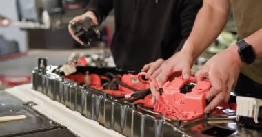 İki teknisyen bir atölyede elektrikli araba aküsü üzerinde çalışıyor. Görüntü, ayrıntılı montaj ve onarım sürecini yakalar. Elektrikli araba. Batarya hücre modülü sürüsü. EV arabası