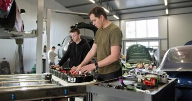 Modern bir atölyede, yüksek voltajlı lityum iyonlu bir pilin montajı ve onarımı için çalışan teknisyenler. Elektrikli araba. Batarya hücre modülü sürüsü. EV arabası