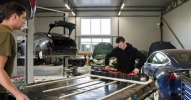 İki teknisyen modern bir otomotiv atölyesinde elektrikli bir araç için yüksek voltajlı lityum iyon batarya paketi hazırlıyorlar. Elektrikli araba. Batarya hücre modülü sürüsü. EV arabası