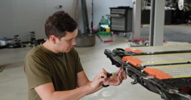 Modern bir atölye ortamında, yüksek voltajlı bir akü paketinin tamiri için çalışan erkek teknisyen. Elektrikli araba. Batarya hücre modülü sürüsü. EV arabası