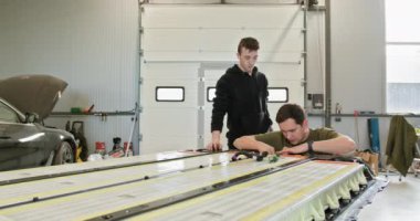 İki erkek teknisyen modern bir araba atölyesinde lityum iyon bataryasını inceliyor ve onarıyor. Teknisyenler atölyedeki elektrikli araba aküsünü tamir ediyor. Elektrikli araba..