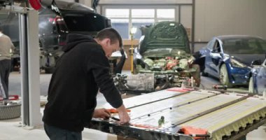 Erkek teknisyen modern bir otomotiv tamirhanesinde yüksek kapasiteli lityum iyonlu bir batarya modülünü tamir ediyor. Araba tamirhanesinde EV pili üzerinde çalışan bir teknisyen.