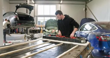 Erkek teknisyen modern bir araba tamir atölyesinde yüksek voltajlı bir aküyü tamir etmeye çalışıyor. Atölyedeki elektrikli araba aküsünü tamir eden teknisyen. Elektrikli araba..