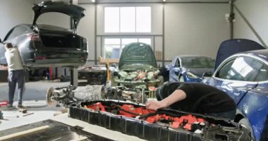 Bir otomotiv atölyesinde elektrikli araba aküsünü tamir etmeye çalışan bir tamirci. Modern tesiste birkaç elektrikli araç hizmet vermektedir. Elektrikli araba. Batarya hücre modülü sürüsü. EV arabası