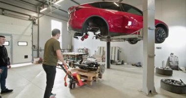 Modern bir garaj atölyesinde parçalanmış bir elektrikli araba üzerinde çalışan iki tamirci. EV bakım ve onarım konsepti. EV onarım konsepti. Otomobil Servisi, Elektrikli Araba Aküsü Taşıma.