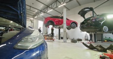 İyi donanımlı modern bir otomotiv atölyesinde, elektrikli araçlar üzerinde bakım ve onarım yapan tamirciler. Araçlar teftiş için kaldırıldı. EV onarım konsepti. Otomobil servisi, elektrikli araba.