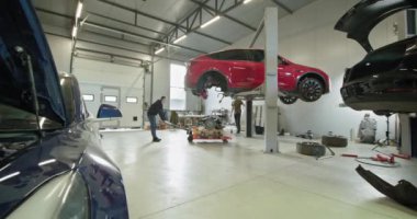 Modern bir servis garajında tamirciler elektrikli araçların bakımını ve tamirini yapıyor. Görüntü, EV bakım, servis ve onarım kavramlarını vurguluyor. EV onarım konsepti. Otomobil servisi, elektrikli araba.