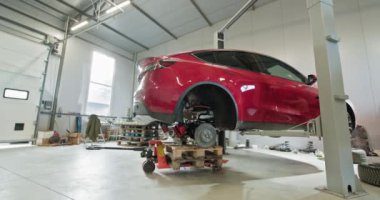 Modern bir atölyede servise verilen kırmızı elektrikli bir araba. Araç bakım ve onarım için asansörle yükseltildi. EV onarım konsepti. Otomobil Servisi, Elektrikli Araba Aküsü Taşıma.