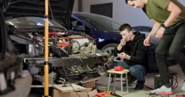 Tamirhanedeki bir arabanın elektrik sorunlarını teşhis eden iki tamirci birlikte çalışıyor. Kesinliği sağlamak için özel aletler ve ekipmanlar kullanıyorlar. Araba elektriği - elektrik tesisatı, voltmetre