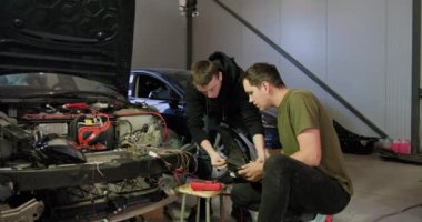 İki tamirci bir oto tamirhanesinde elektrik sistemini tamir etmeye çalışıyor. Ellerinin ve aletlerinin detaylı çekimleri, teknik uzmanlık göstergesi. Otomobil servisi atölyesi.