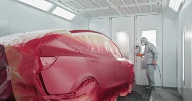 Otomotiv teknisyeni araba bakım merkezindeki özel bir odaya sprey boyayla araba boyuyor. Düzgün bir son için uzman araba boyama işlemi devam ediyor. Bir Araca Boya Uygulayan Araba Boyacısı