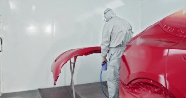Otomotiv teknisyeni özel bir odanın içindeki araba tamponuna boya sürüyor. Araba tamirhanesinde profesyonel araba boyama servisi. Araba Boyacısı Oto Tamirhanesinde Kaplama Tamponunda.